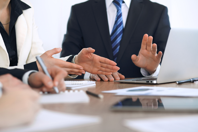Group of businesspeople or lawyers discussing contract papers and financial figures while sitting at the table. Close-up of human hands at meeting or negotiations. Success and communication concept.